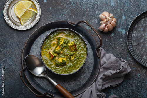 Traditional Indian Punjabi food Palak Paneer with spinach and cheese in vintage metal bowl with spoon on rustic concrete background from above 