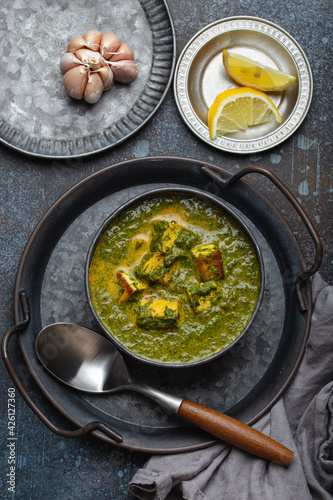 Traditional Indian Punjabi food Palak Paneer with spinach and cheese in vintage metal bowl with spoon on rustic concrete background from above 