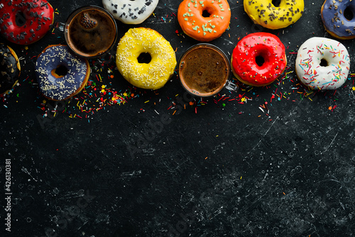 Set of sweet colored donuts with a cup of coffee on a black stone table. Top view. Flat Lay.