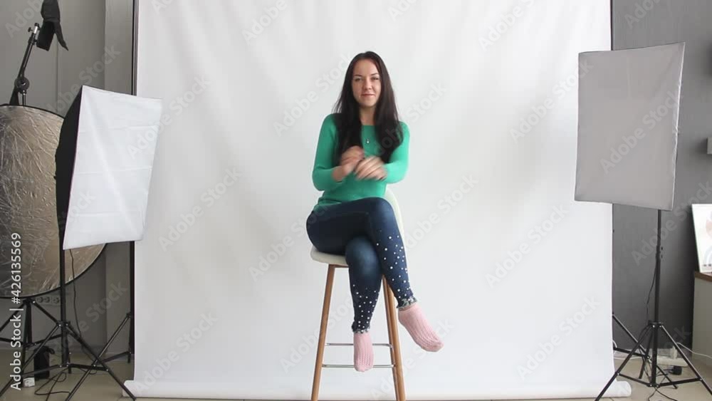 the girl entered the frame. young brunette woman in jeans and green shirt is sitting on the white background in the home photo studio. making off video, lifestyle concept