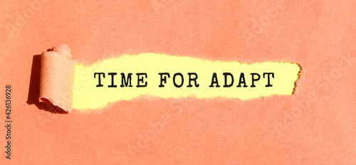 The text TIME FOR ADAPT appearing on yellow paper behind torn color paper. Top view.