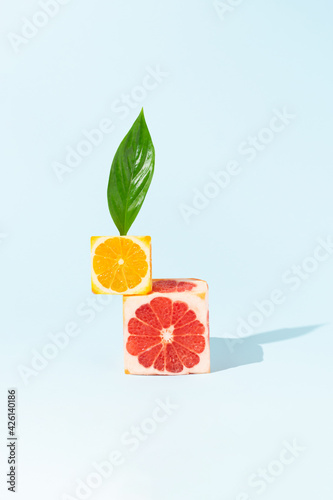 Fototapeta Naklejka Na Ścianę i Meble -  Creative fruit composition made with orange and grapefruit cube slices with sunlight shadow against bright blue background. Minimal food concept.