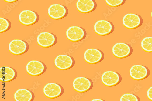 Minimal fruit pattern made with yellow lemon slices with sunlight shadow on bright orange background. Creative food concept.