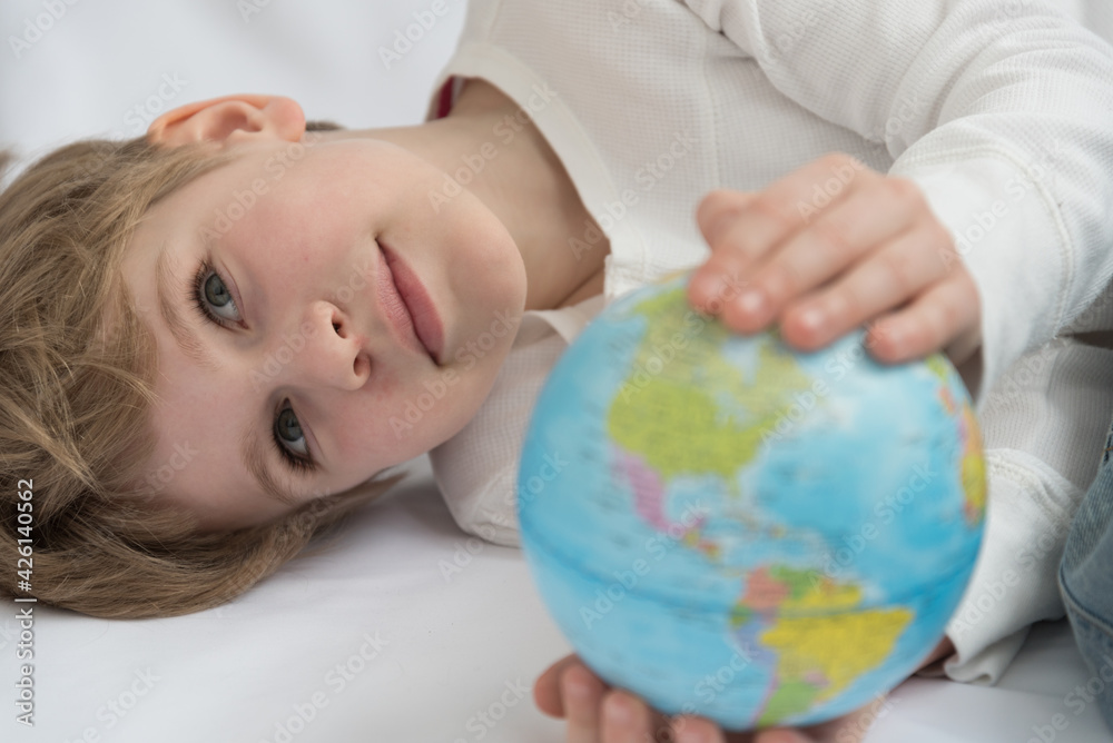 The child dreamily examines the globe. Travel yearning concept. Closed borders and quarantine. A European-looking child dreams of travel The child dreamily examines the globe. Travel yearning concept. Closed borders and quarantine. A European-looking child dreams of travel