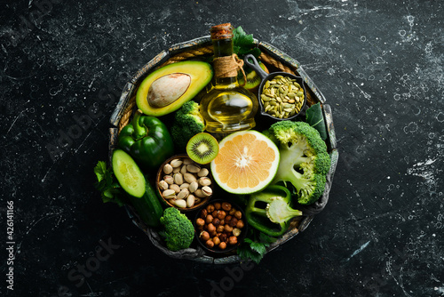 Green vegetables, fruits and nuts: avocado, broccoli, pistachios, parsley, celery, cucumber and kiwi. Top view. Rustic style.