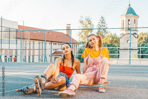 Two teen girls, friends in colorful clothes with roller skates and skate board. © stivog