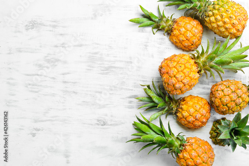 Pineapple white background. Ripe baby pineapple on a white wooden background. Tropical fruits. Top view. Free space for text.