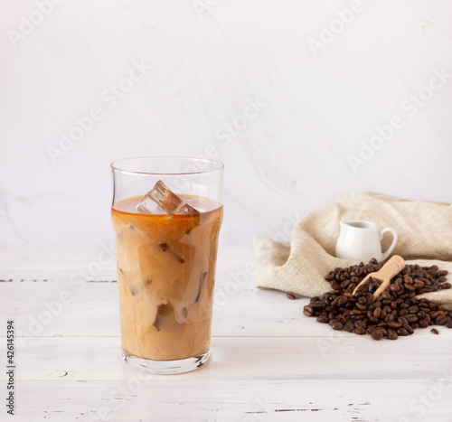 A glass cup with cold coffee and ice, coffee beans on a light background.
