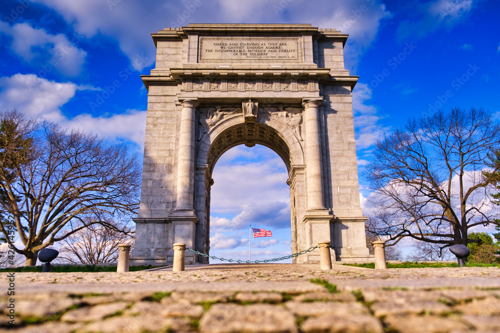 The National Memorial Arch stands with the American Flag blowing in the middle at Valley Forge National Park in Pennsylvania.