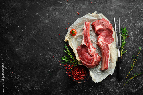 Fresh raw veal steak on the bone with rosemary and spices. On a black stone background. Top view.