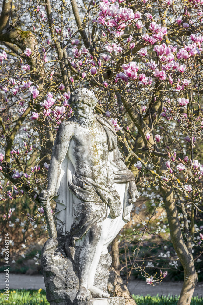 Fototapeta premium Statue von Pluto vor einem blühenden Magnolienbaum im Palmengarten von Frankfurt