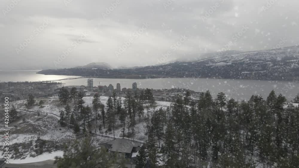 Drone Aerial View, Blizzard Above Kelowna, Canada, Snow Capped Hills and Forest by Okanagan Lake on Cloudy Winter Day Drone Aerial View, Blizzard Above Kelowna, Canada, Snow Capped Hills and Forest by Okanagan Lake on Cloudy Winter Day