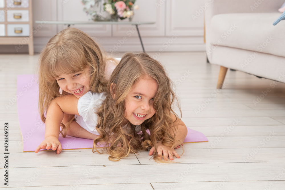Horizontal photo of couple little girls playing on yoga mat smiling Horizontal photo of couple little girls playing on yoga mat smiling