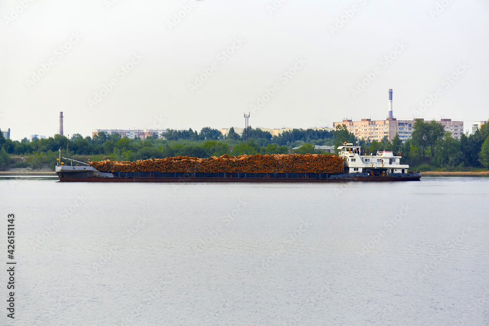 river timber carrier ship loaded with logs moves past the urban coast