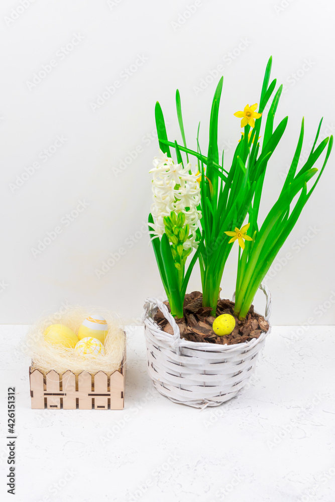 Obraz premium Easter concept. Yellow Easter eggs in a nest next to a bouquet of daffodils on a white concrete table. Place for an inscription. Base for coating.