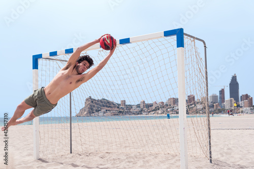Diagonal perspective of a soccer goalkeeper on the beach stopping a ball.