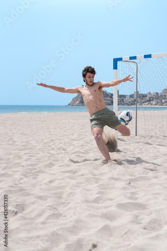 A young goalkeeper playing on the beach pulls the ball out hard.