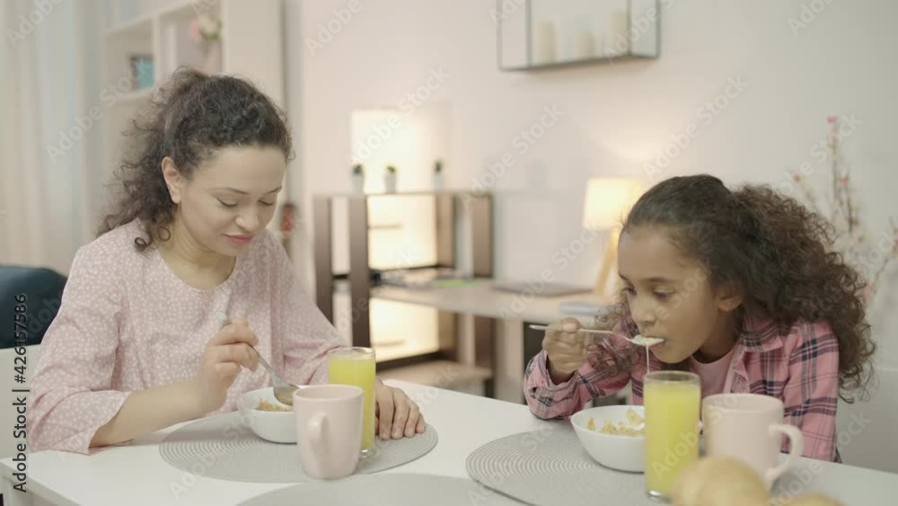 Cheerful mother and daughter eating at home, talking and enjoying family time Cheerful mother and daughter eating at home, talking and enjoying family time