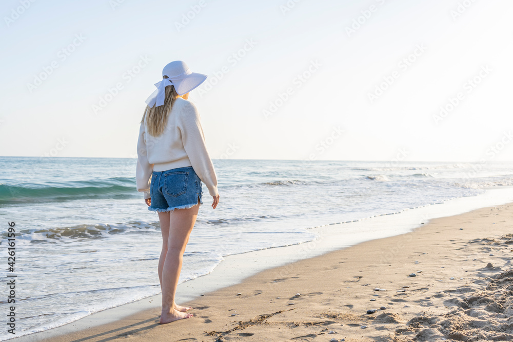 Stylish beautiful young woman walking on the beach enjoying the ocean at sunset.Summer holidays concept lifestyle with copy space for text.