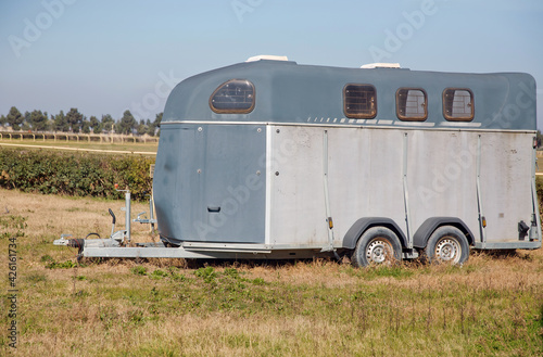 silver horse trailer on green weadow . A trailer used for transporting one adult horse A trailer used for transporting one adult horse. A horse trailer with graphics is ready to hook up and go .