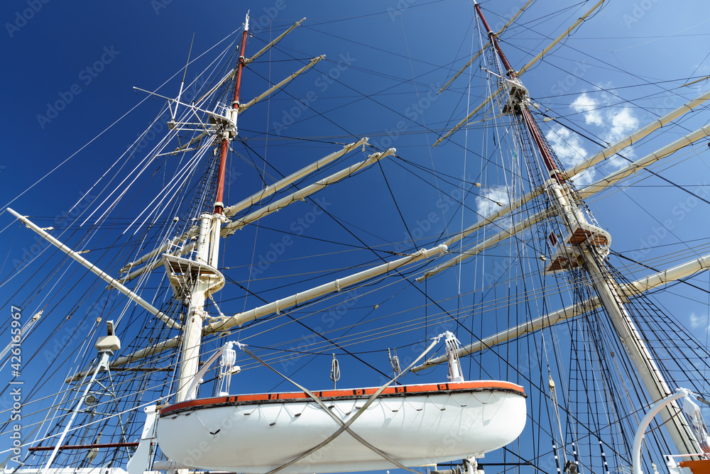 Masting and rigging of an old classical sailing boat with a lifeboat against a blue sky
