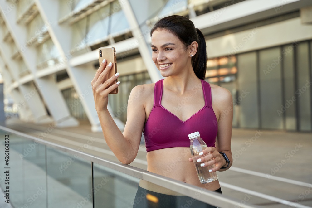 Happy young woman holding smartphone and bottle of water