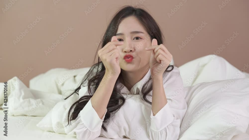 Cheerful young woman lying on bed playing with blanket and looking at camera. Asian girl feeling fresh after nap on bed. Cute woman having fun while embracing pillow. Cheerful young woman lying on bed playing with blanket and looking at camera. Asian girl feeling fresh after nap on bed. Cute woman having fun while embracing pillow.