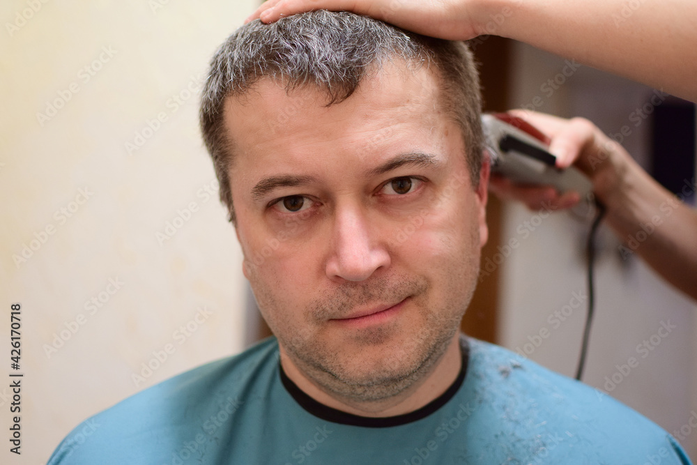 Fototapeta premium A man is trimmed with a hair clipper and sits facing the camera. Perhaps at home in a lockdown