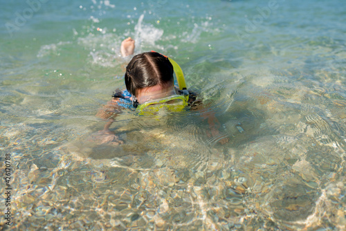 Close up of toddler girl learning snorkeling on shallows. Child immersing the head in water. Kids diving with snorkel mask and tube on the water s edge. Family vacation concept