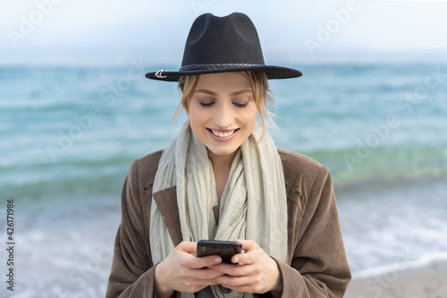 Stunning young woman holding a mobile phone with a smile while texting a massage 
