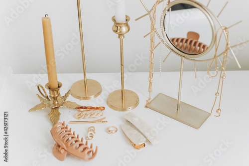 Modern gold jewellery, hair clips on white table with vintage candles and boho mirror. Accessories