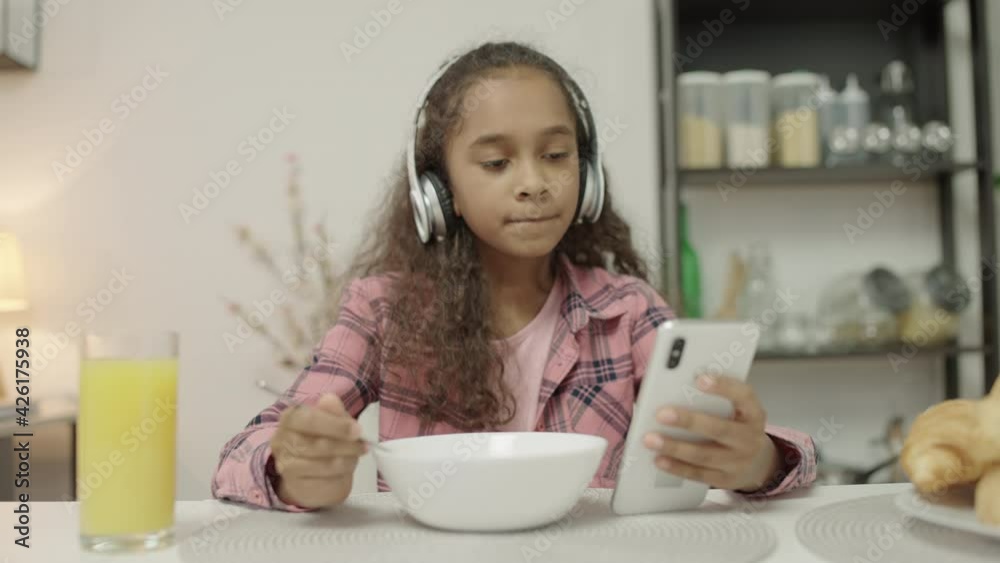 Teen girl having meal in earphones scrolling smartphone, unhealthy eating habits Teen girl having meal in earphones scrolling smartphone, unhealthy eating habits