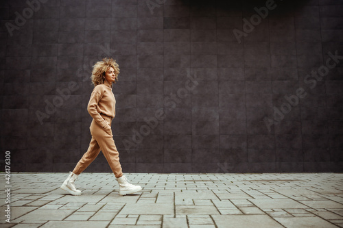 Side view of trap girl in tracksuit walking with hands in her pockets and listening music. photo
