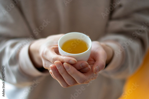woman holding cup of tea in her hands. No face, blurred background.