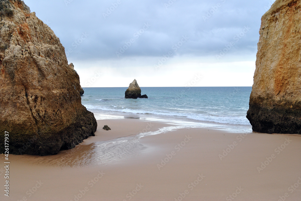 Deserted Wet Sandy Beach with Exposed Rocks and Cliff 