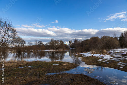 River flood on a spring day. Dry grass is visible from under the snow. The land is flooded with water.