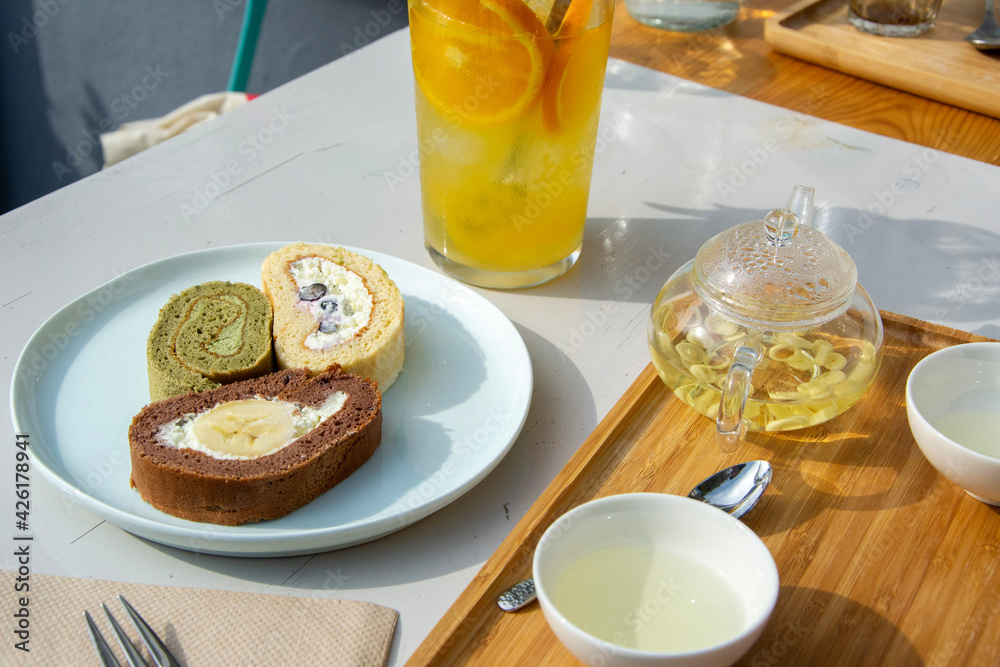 matcha, vanilla and chocolate banana swiss roll cake slices with green tea and orange lemonade in a cafe