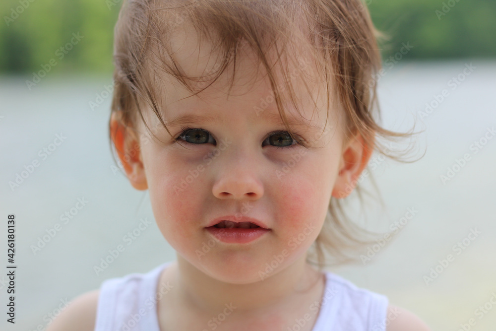 Happy little girl with gray eyes and curly blond hair in a white T-shirt stands on the river bank Happy little girl with gray eyes and curly blond hair in a white T-shirt stands on the river bank