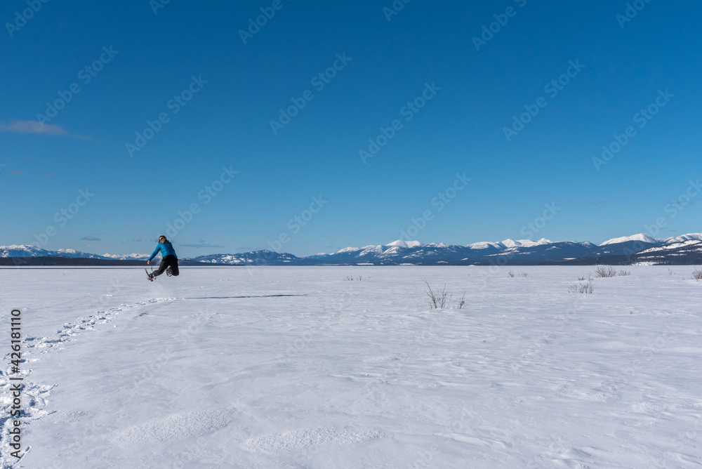 Man jumping with joy on a frozen river in northern Canada during spring time wearing snowshoes and stunning blue sky background. 
