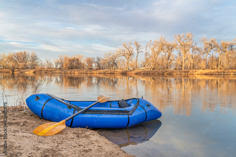 inflatable packraft (one-person light raft used for expedition or adventure racing) with a paddle on a lake shore in Colorado, early spring scenery inflatable packraft (one-person light raft used for expedition or adventure racing) with a paddle on a lake shore in Colorado, early spring scenery