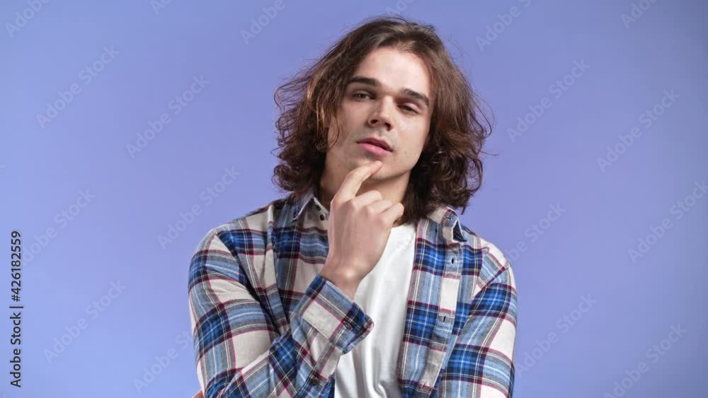Thinking man looking up on violet background. Pensive face expressions. Handsome man with long hairdo in plaid shirt