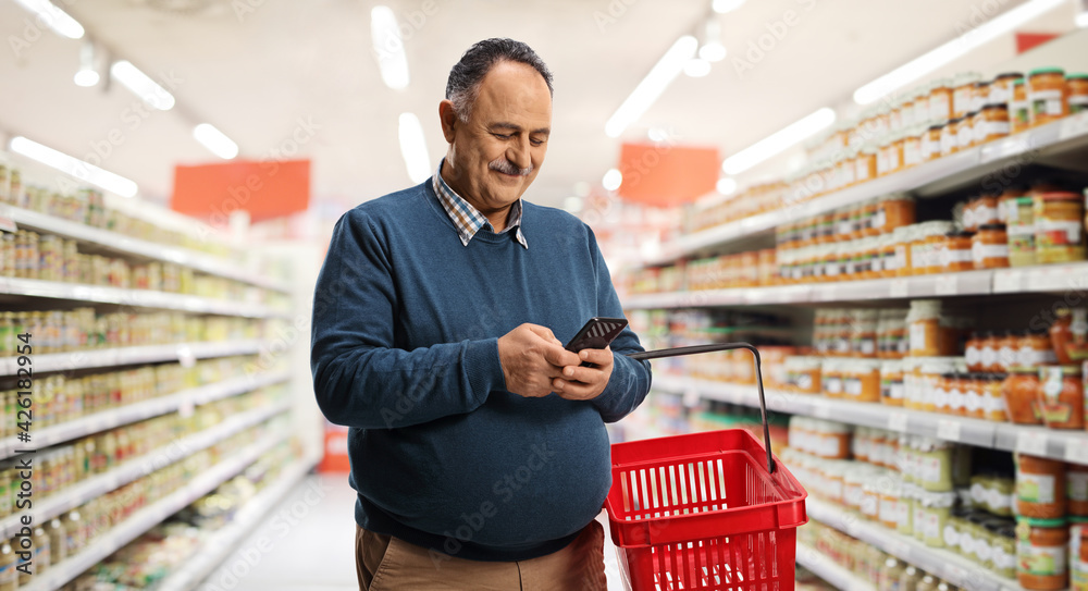 Mature man with a shopping basket typing on a smartphone
