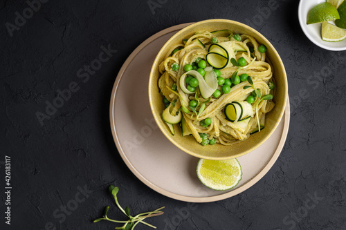 Bowl of linguine pasta with avocado sauce, green peas, zucchini, sprouts on dark grey table
