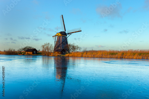 Windmills at Kinderdijk, close to Rotterdam in The Netherlands, in winter with ice on canal at sunset.