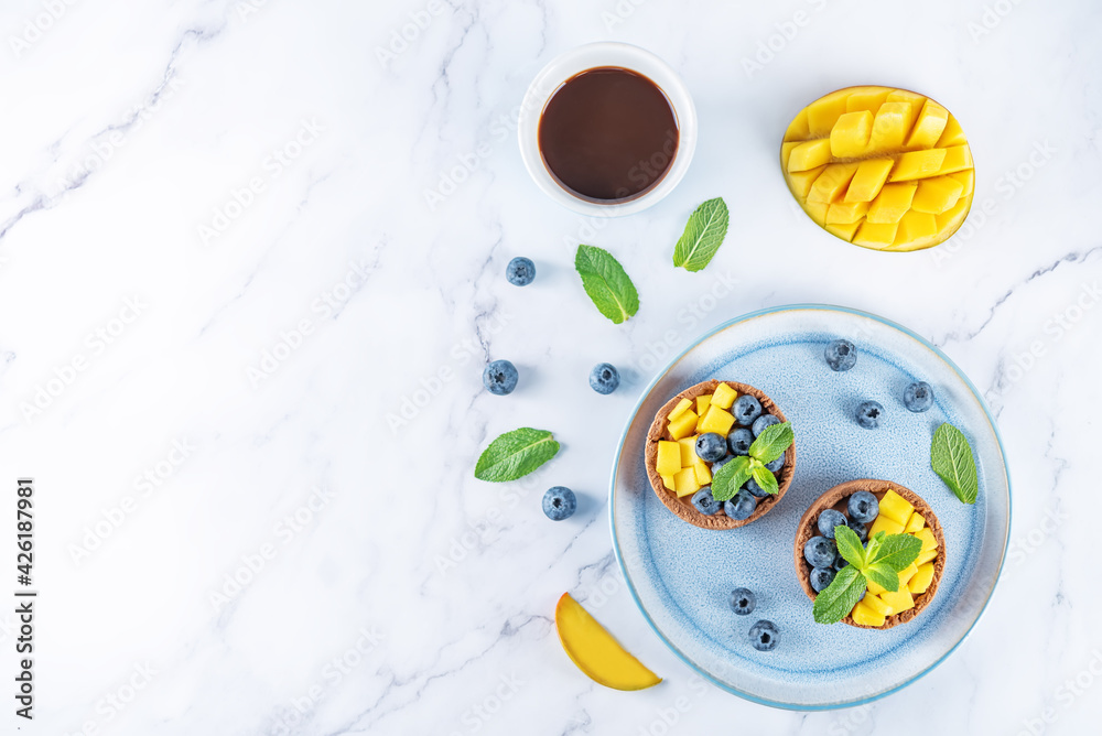 Chocolate tartlets with chocolate cream filling and mango fruit with blueberries