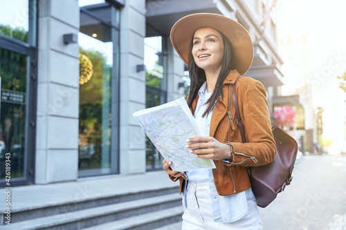 Young lady in hat using map while walking outdoor