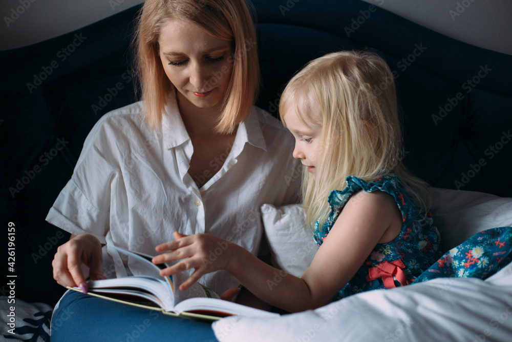 Happy family of blonde mom and daughter are reading a book in bed. Happy family of blonde mom and daughter are reading a book in bed.