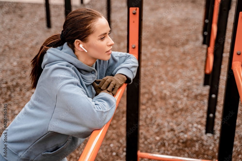 Obraz premium Young woman in sports outfit doing morning workout outdoors. Cute female resting after pulling up on street sports ground. Staying fit and healthy concept