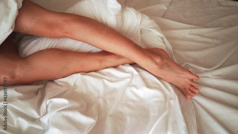 Beautiful female legs gracefully move in bed in the morning. Body care concept. Top view. Beautiful female legs gracefully move in bed in the morning. Body care concept. Top view.