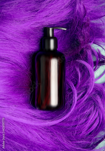 Dark bottle of shampoo on purple hair, top view